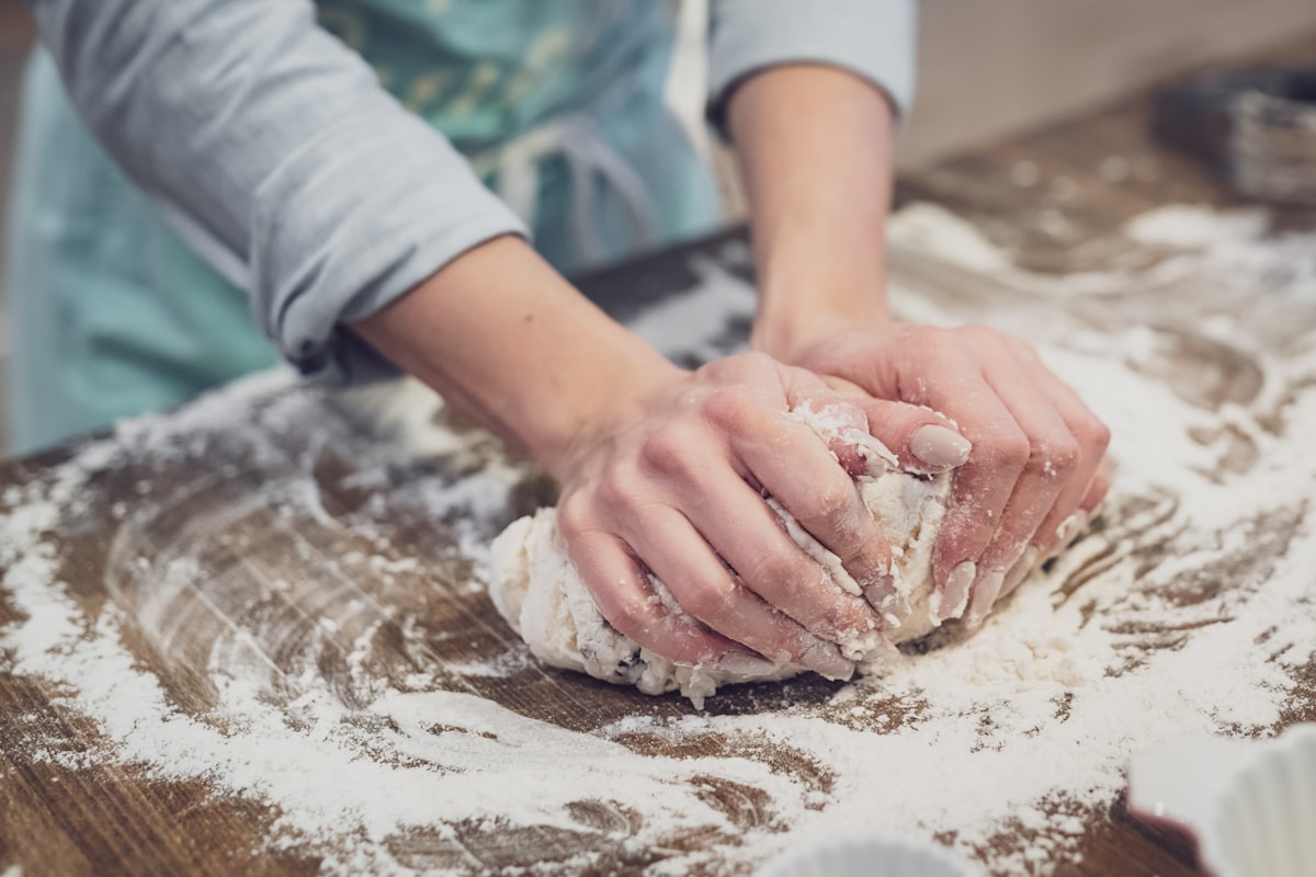 Handen kneden brooddeeg op een bebloemd houten werkblad in Bakkerij De Desemhoek